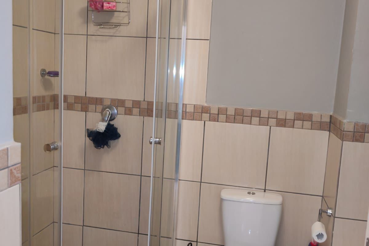 A functional bathroom featuring a glass-enclosed shower, a standard toilet, and neutral ceramic wall tiling with a decorative mosaic border.