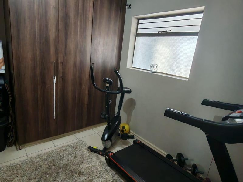 A bedroom featuring dark wood-finish built-in cupboards, tiled flooring, and a louvered window providing natural light.