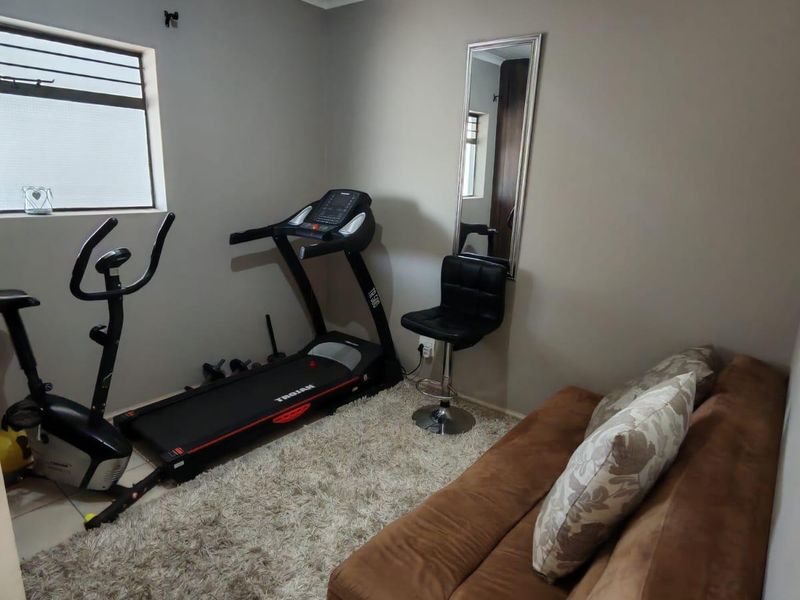A functional home gym space featuring neutral wall finishes, tiled flooring, and ceiling-mounted track lighting, currently utilized as a multi-purpose exercise and relaxation area.