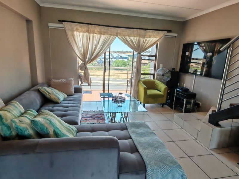 A bright living room featuring tiled flooring, a staircase with metal railings, and a sliding glass door leading to an outdoor balcony area.