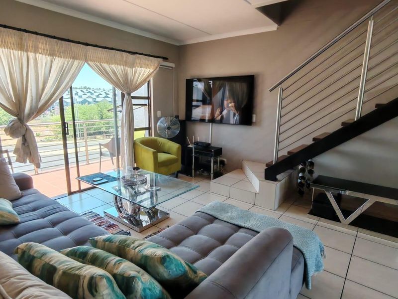 Open-plan living area featuring tiled flooring, a modern staircase with stainless steel balustrades, and large sliding glass doors leading to a balcony.