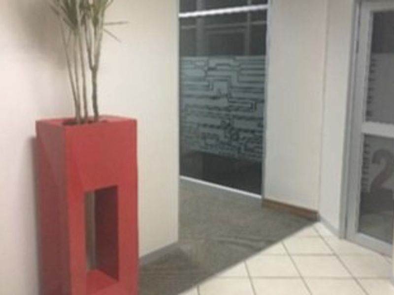 A commercial hallway featuring a mix of tiled and carpeted flooring, leading to a glass office door and a frosted glass partition.