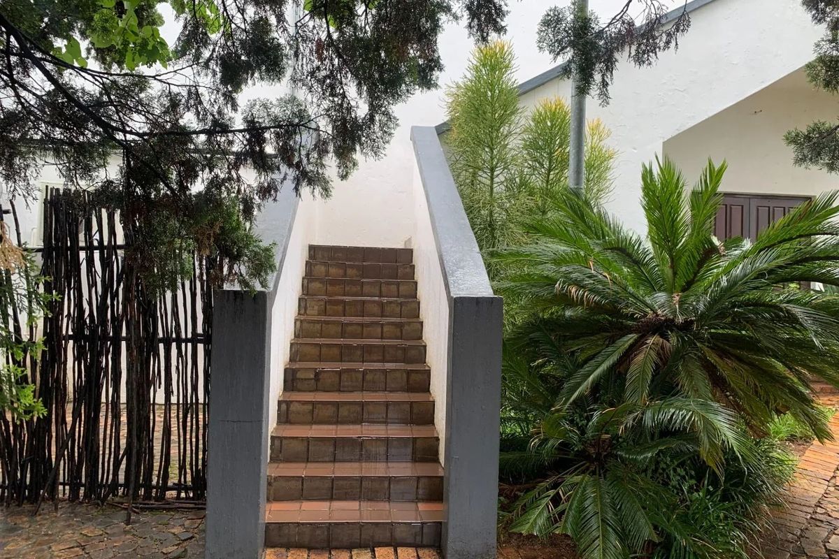 An exterior view of a tiled staircase leading to an upper level, featuring concrete balustrades and surrounding landscaped garden area.