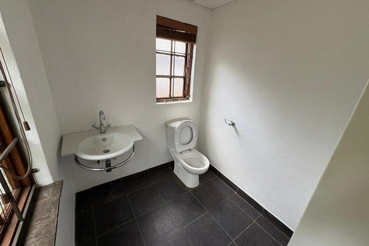 A functional guest bathroom featuring a wall-mounted basin, toilet, dark tiled flooring, and a timber-framed window.