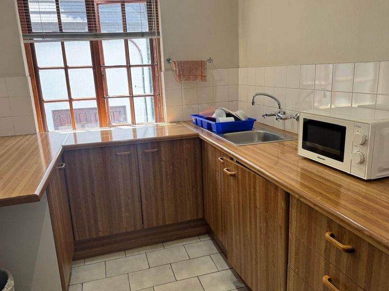 A functional scullery area featuring wood-finish cabinetry, laminate countertops, a stainless steel sink, and tiled splashbacks, providing practical prep and wash-up space.