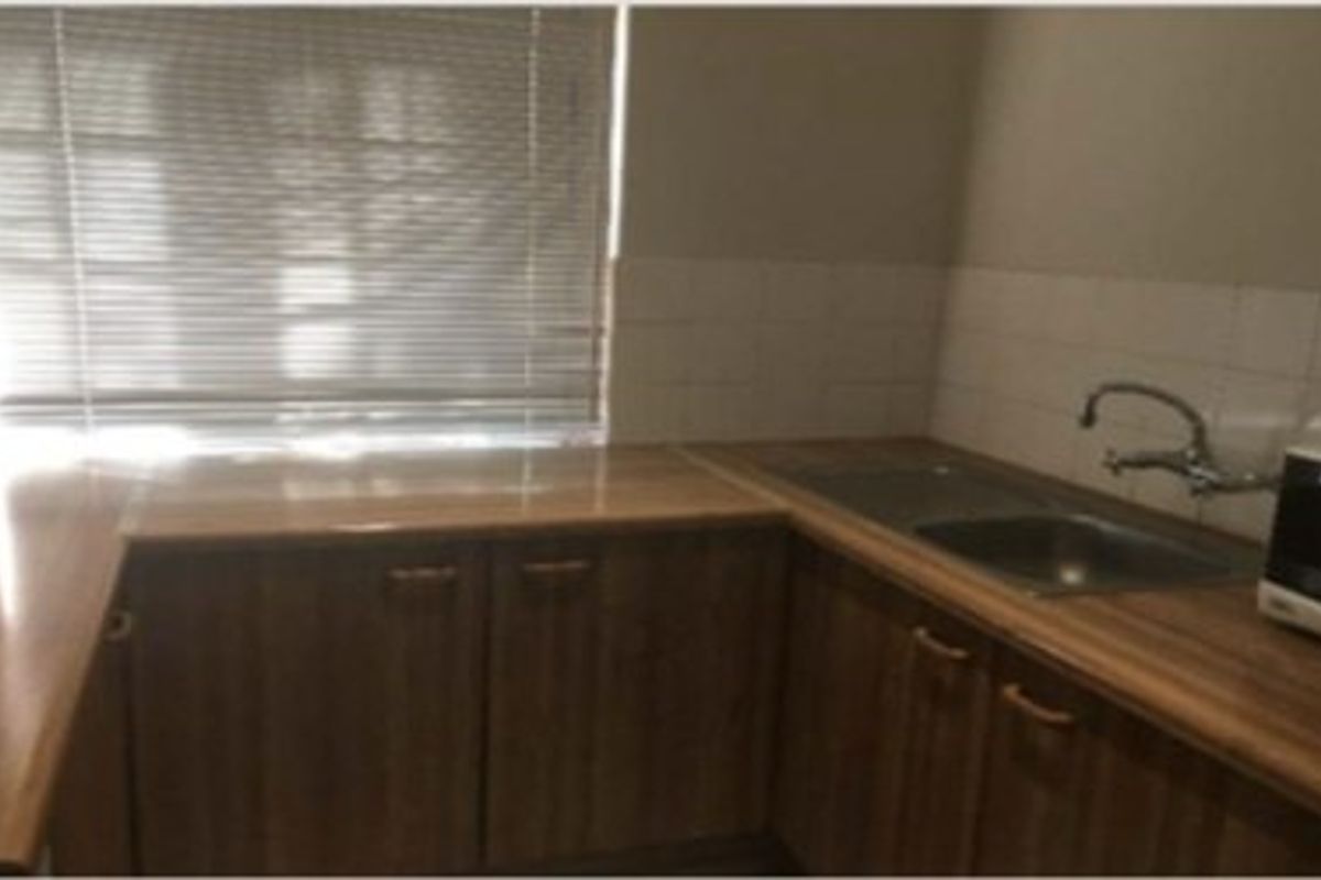 A functional kitchen area featuring laminate countertops, a double basin sink with mixer tap, and tiled splashbacks, providing a practical workspace.