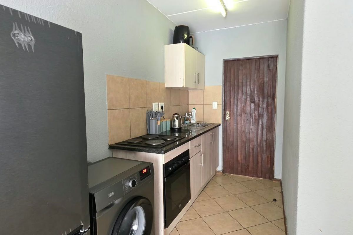 Compact kitchen featuring built-in cabinetry, electric hob, oven, and tiled backsplash, providing a functional workspace with tiled flooring.