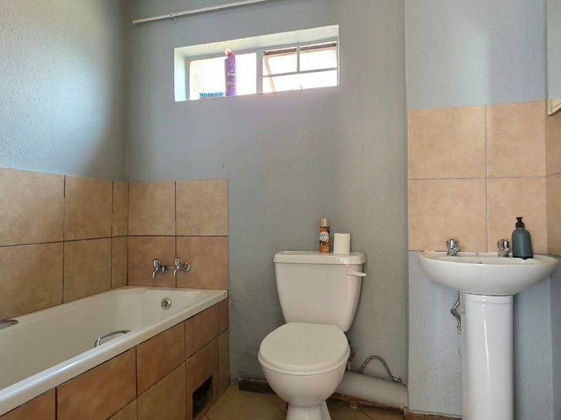 A functional bathroom featuring a bathtub, pedestal basin, and toilet with tiled splashbacks, requiring minor maintenance to the bathtub apron and exposed plumbing.