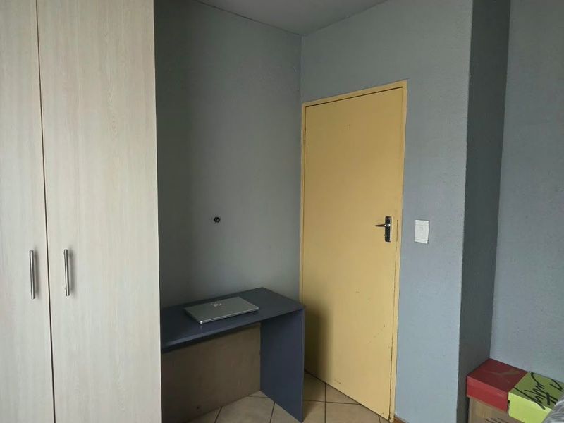 A bedroom featuring a light wood-finish built-in wardrobe, tiled flooring, and neutral wall tones, offering a functional space for rest or study.
