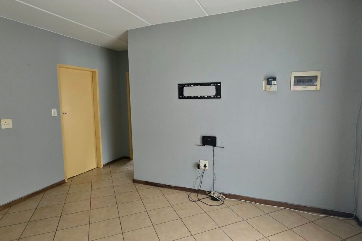 An empty living room featuring tiled flooring, a wall-mounted TV bracket, and an intercom system, providing a blank canvas for personalization.
