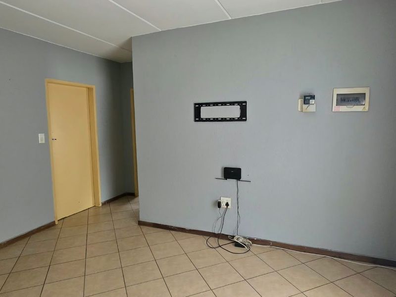 An empty living room featuring tiled flooring, a wall-mounted TV bracket, and an intercom system, providing a blank canvas for personalization.