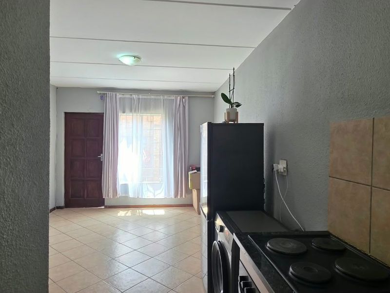 An open-plan living and kitchen area featuring tiled flooring, a built-in stove with a tiled backsplash, and natural light from the window.