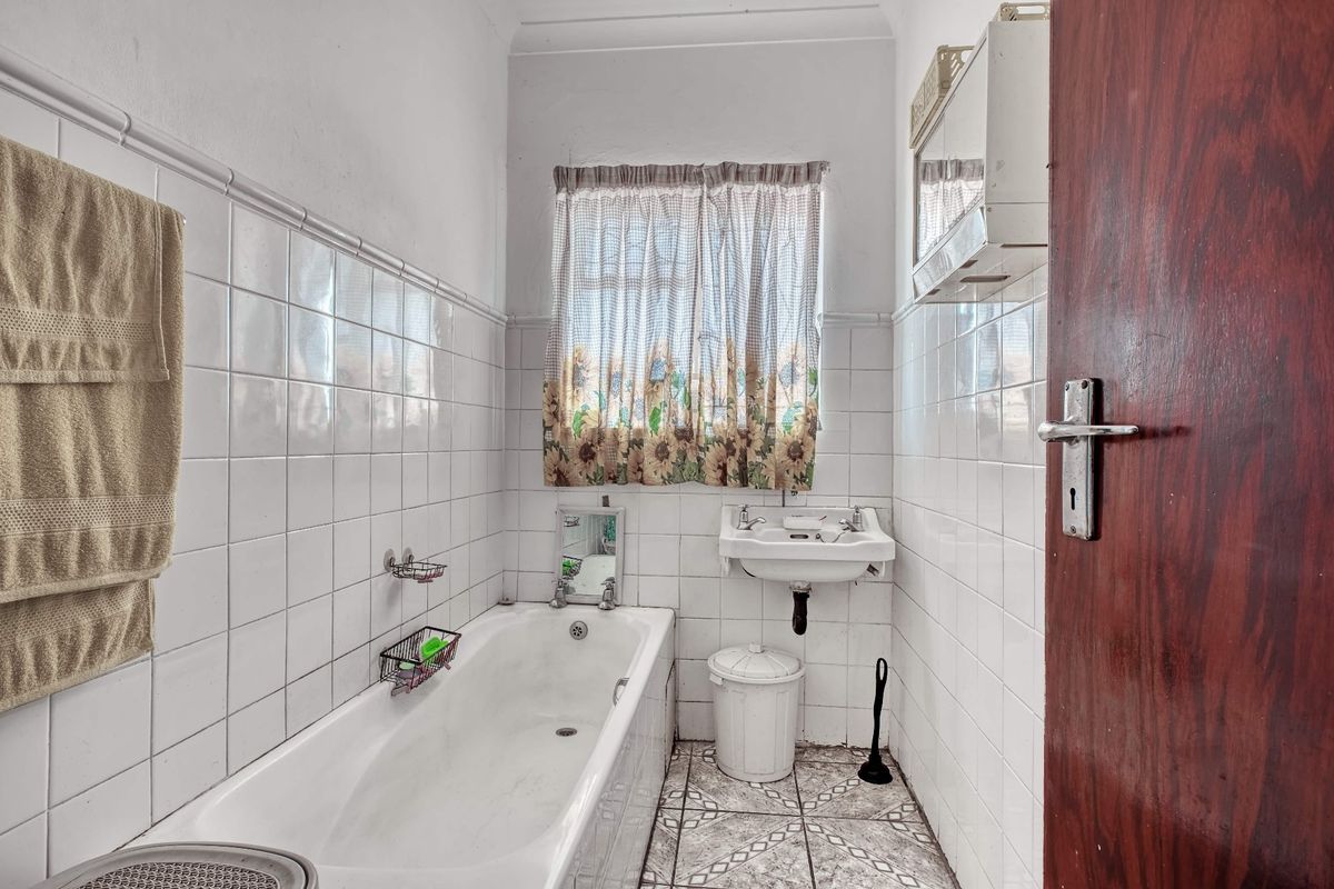 A compact bathroom featuring a standard bathtub, wall-mounted basin, and tiled finishes, offering potential for a modern renovation.