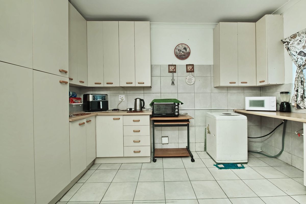 A functional kitchen featuring built-in cabinetry, tiled backsplash, and tiled flooring, offering a practical layout with space for laundry appliances.