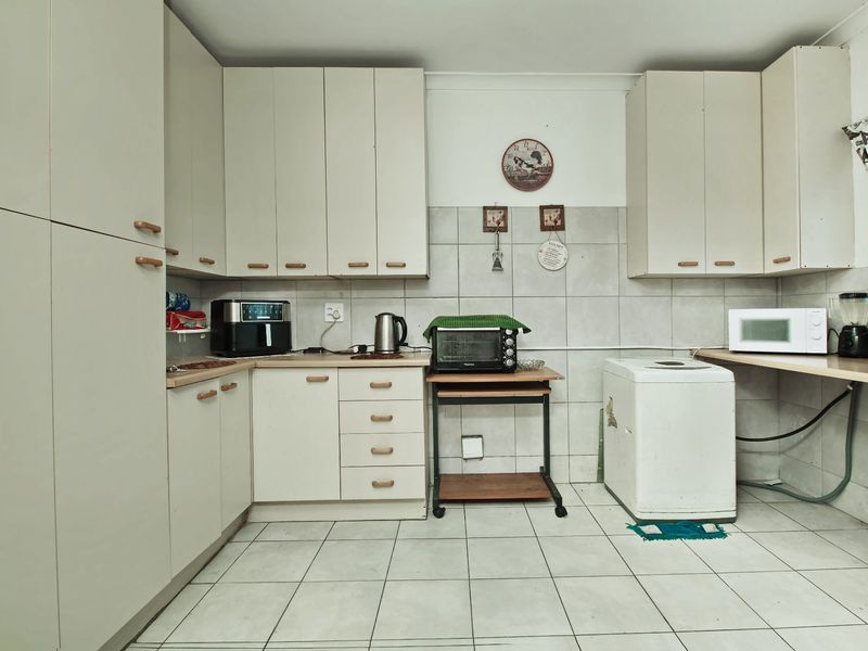 A functional kitchen featuring built-in cabinetry, tiled backsplash, and tiled flooring, offering a practical layout with space for laundry appliances.
