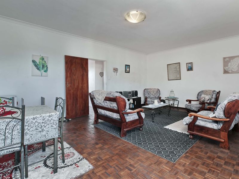 Spacious living area featuring classic parquet flooring and a neutral color palette, offering a versatile layout for comfortable seating and dining arrangements.
