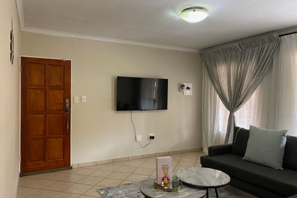 A comfortable living room featuring tiled flooring, a timber panel door, and neutral wall finishes, providing a functional and well-lit space.