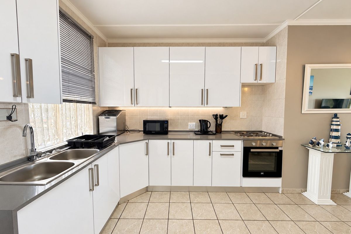 Modern kitchen featuring white high-gloss cabinetry, stainless steel sink, built-in oven, gas hob, and neutral tiled flooring with a clean, functional layout.