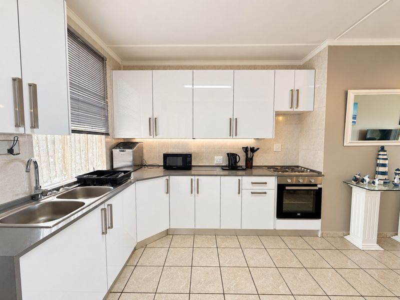 Modern kitchen featuring white high-gloss cabinetry, stainless steel sink, built-in oven, gas hob, and neutral tiled flooring with a clean, functional layout.