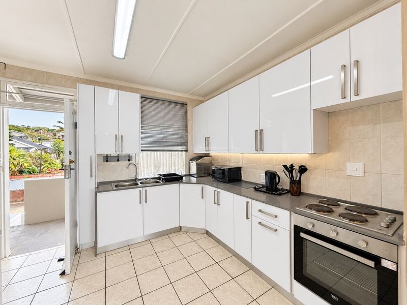 A functional kitchen featuring white gloss cabinetry, a tiled backsplash, integrated electric hob and oven, and direct access to an outdoor balcony area.