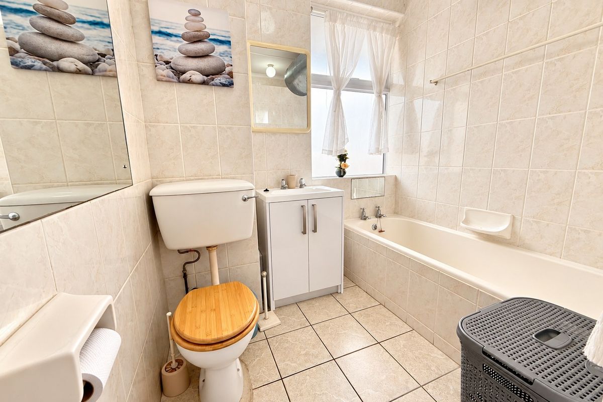 A functional bathroom featuring a bathtub, built-in vanity cabinet, and neutral ceramic tiling throughout.