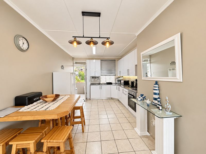Open-plan kitchen and dining area featuring modern white cabinetry, tiled flooring, and integrated appliances, creating a functional and bright living space.