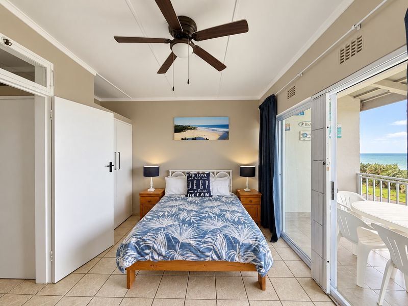 A bedroom featuring tiled flooring, a ceiling fan, and a built-in wardrobe, with direct access to a balcony through sliding glass doors.