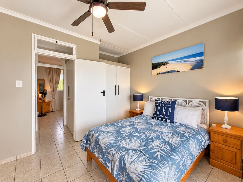 A well-maintained bedroom featuring tiled flooring, a ceiling fan, and built-in cupboards, with an adjoining hallway visible through the doorway.