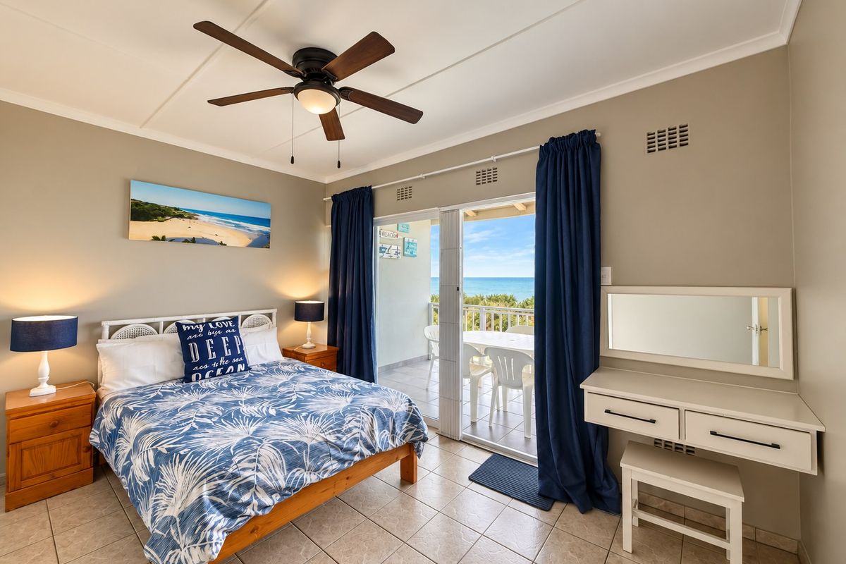 A well-maintained bedroom featuring tiled flooring, a ceiling fan, and direct access to a balcony with ocean views through sliding glass doors.