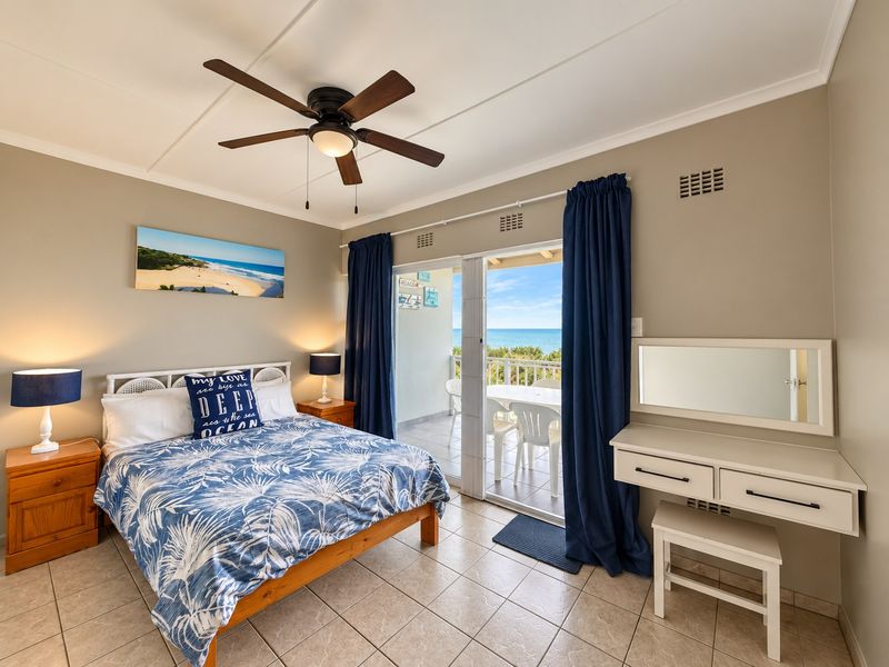 A well-maintained bedroom featuring tiled flooring, a ceiling fan, and direct access to a balcony with ocean views through sliding glass doors.
