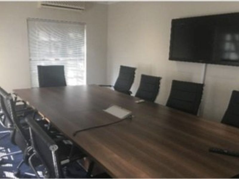 A functional office boardroom featuring a wall-mounted television, air conditioning unit, and window blinds, suitable for professional meetings and collaborative work.