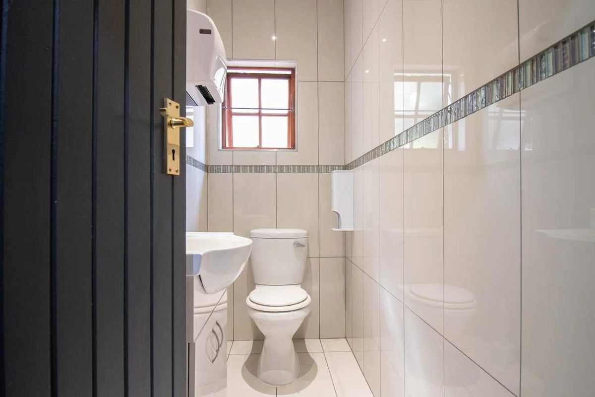 A clean and well-maintained guest bathroom featuring neutral wall tiles, a decorative border, a pedestal basin, and a standard toilet.