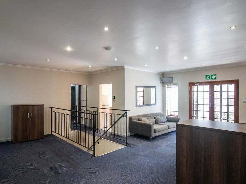 Spacious commercial office area featuring recessed lighting, a metal balustrade staircase, and direct access to an exterior entrance.