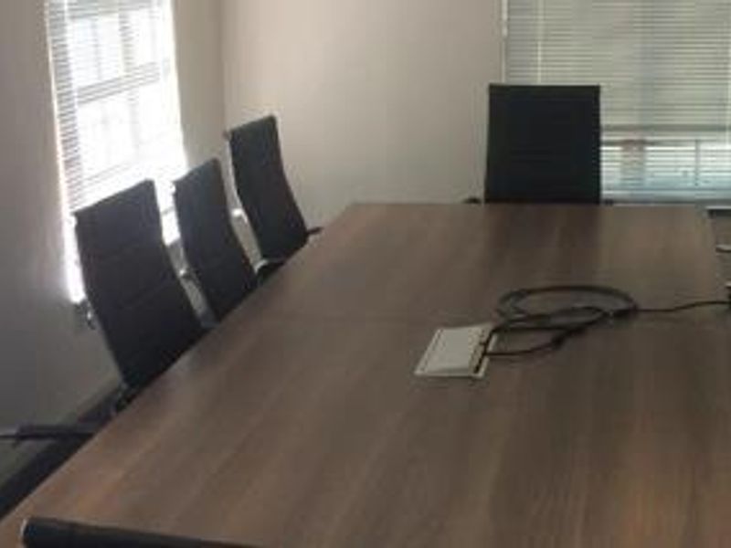 A functional office meeting room featuring large windows with venetian blinds and integrated power connectivity.