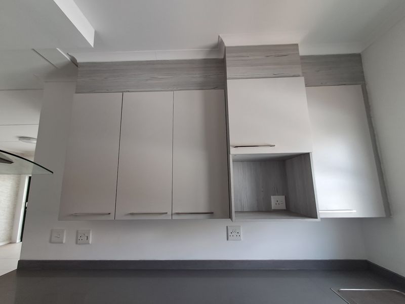 A modern kitchen area featuring clean, neutral-toned built-in cabinetry, a sleek countertop, and integrated electrical outlets.