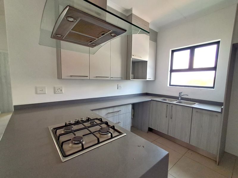 A modern, clean kitchen featuring light wood-grain cabinetry, stone countertops, a gas hob with an extractor fan, and a double sink with a mixer tap.