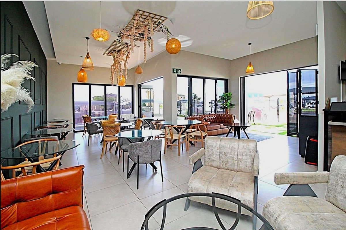 Spacious open-plan living area featuring large format floor tiles, modern feature wall paneling, and expansive black aluminium stacker doors leading to the outdoors.