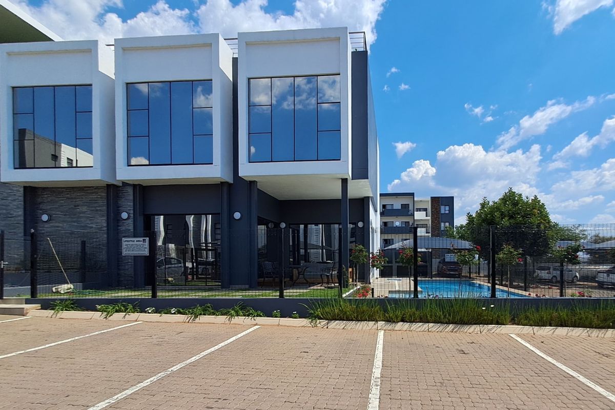Modern apartment complex exterior featuring large glass windows, a swimming pool, and a paved parking area.