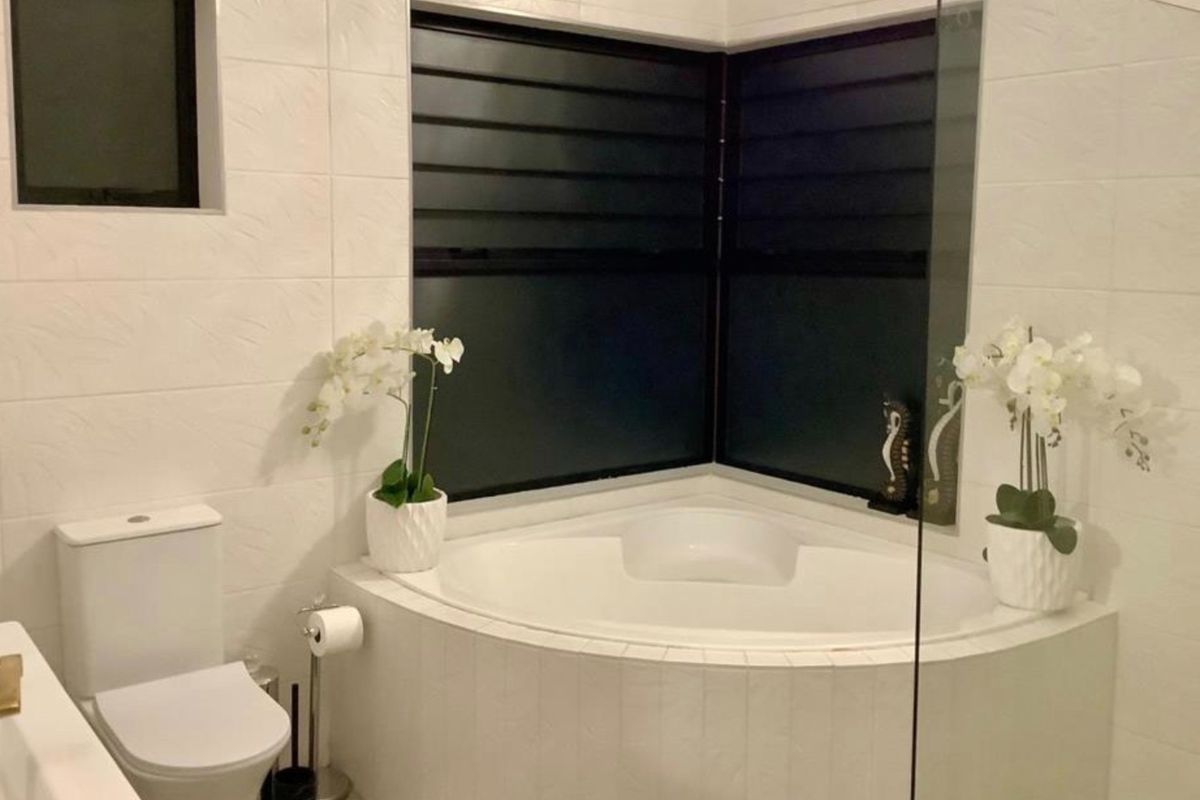 Modern bathroom featuring a corner bathtub, tiled walls, and a glass shower screen, providing a clean and functional space.