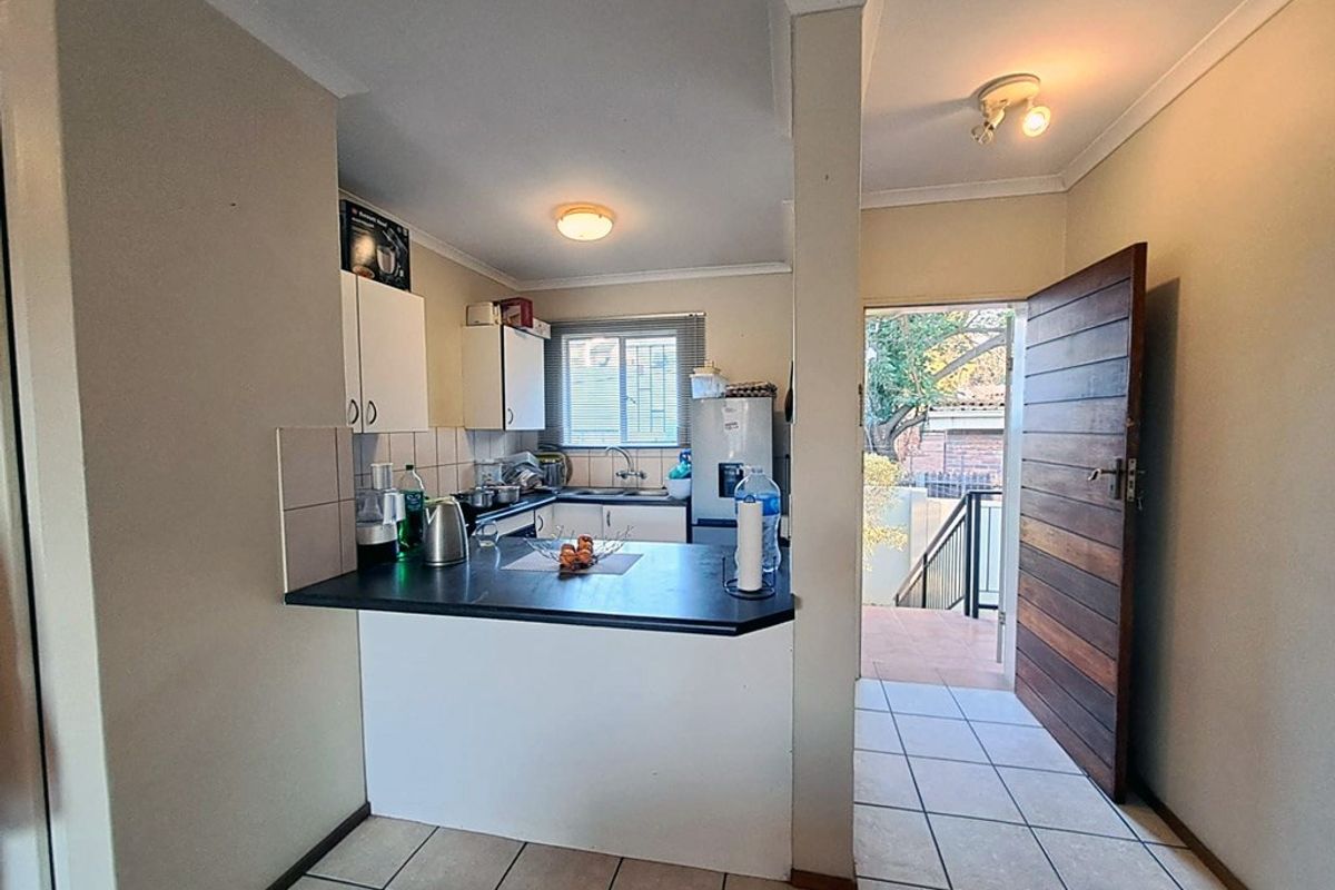 Compact kitchen featuring built-in cabinetry, laminate countertops, and tiled flooring, with direct access to an exterior entrance area.
