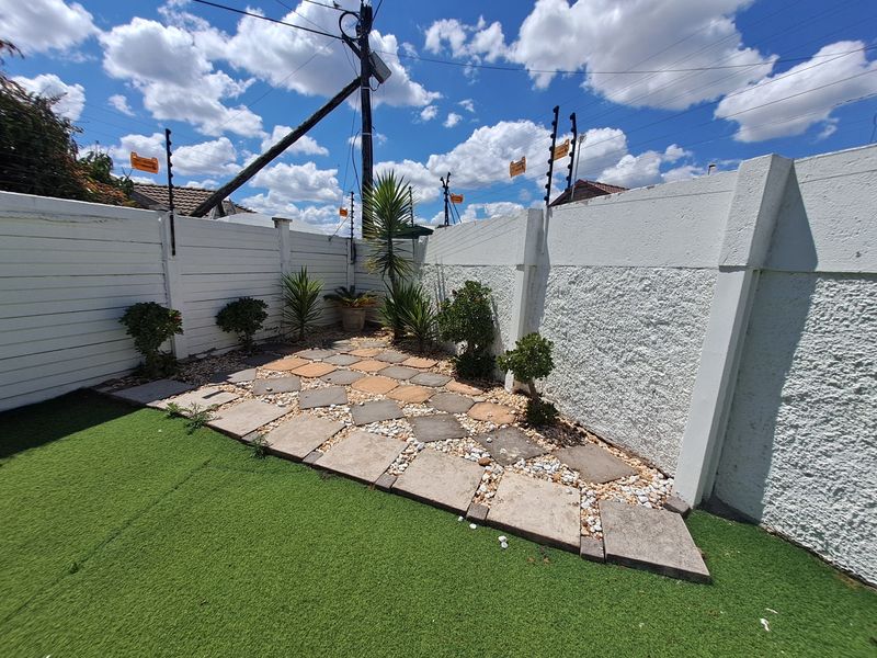 A low-maintenance garden area featuring artificial grass, a paved walkway with pebble accents, and secure perimeter walls with electric fencing.