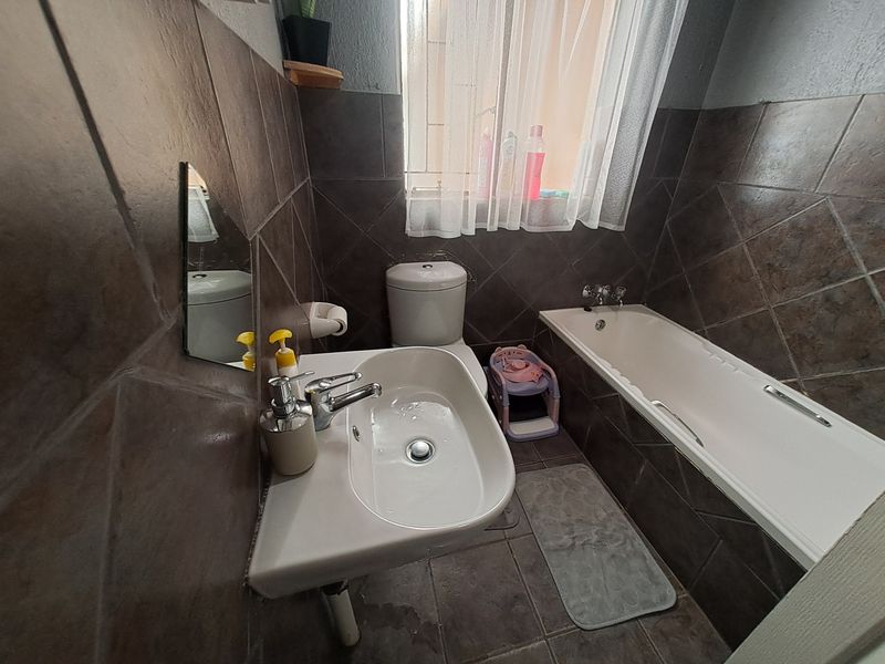 A compact bathroom featuring dark tiled walls and floors, a pedestal basin, a standard toilet, and a bathtub with chrome fixtures.
