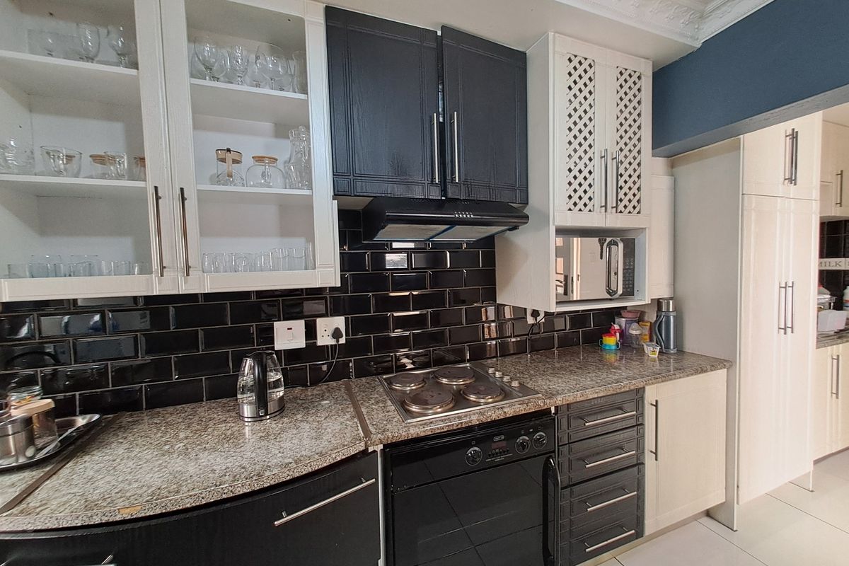 Modern kitchen featuring granite countertops, black subway tile backsplash, built-in oven, hob, extractor fan, and ample cabinetry with decorative glass-fronted display units.