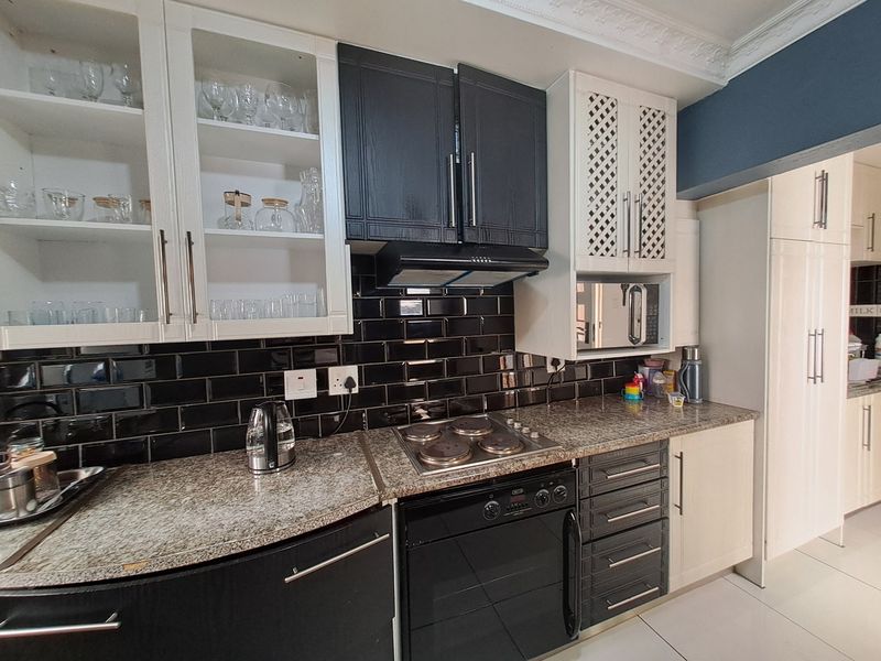 Modern kitchen featuring granite countertops, black subway tile backsplash, built-in oven, hob, extractor fan, and ample cabinetry with decorative glass-fronted display units.