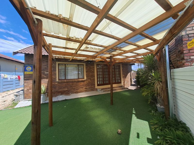 Covered patio area featuring a timber pergola structure with corrugated roofing, facebrick exterior walls, and access to the home via timber-framed sliding doors.