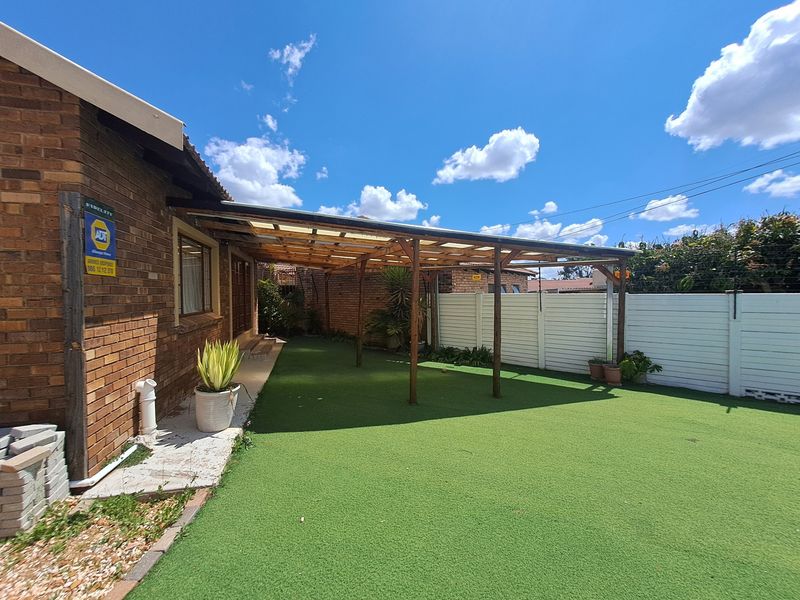 A covered outdoor patio area featuring a timber pergola with polycarbonate roofing, overlooking a low-maintenance artificial lawn and enclosed by a precast boundary wall.