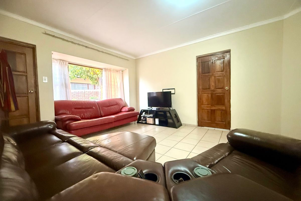 A spacious living room featuring ceramic tile flooring, a large bay window, and traditional solid wood panel doors.