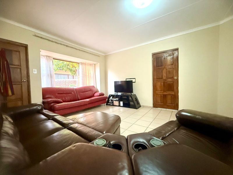 A spacious living room featuring ceramic tile flooring, a large bay window, and traditional solid wood panel doors.