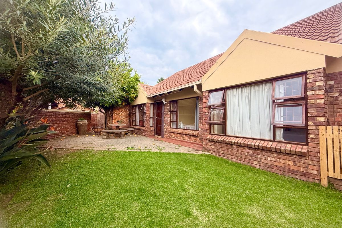 Rear view of the townhouse featuring a face brick facade, tiled roof, paved patio area, and a well-maintained lawn.
