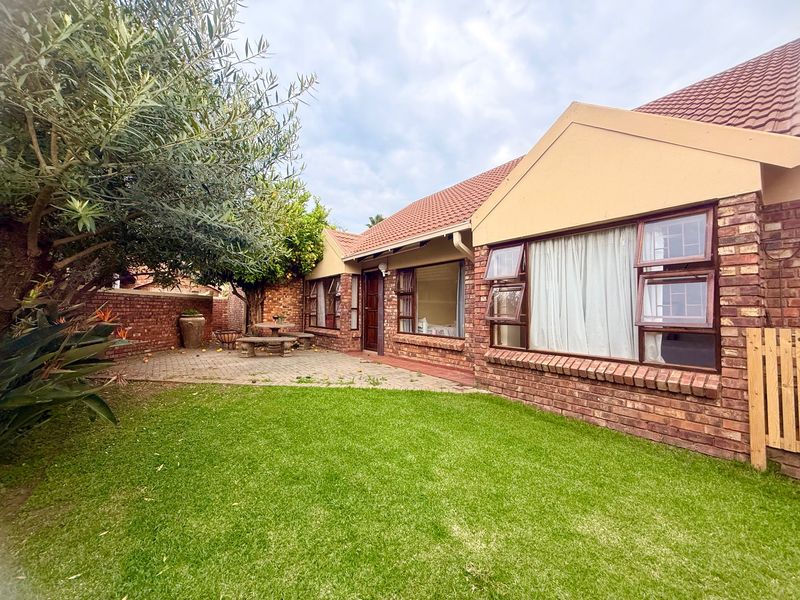Rear view of the townhouse featuring a face brick facade, tiled roof, paved patio area, and a well-maintained lawn.
